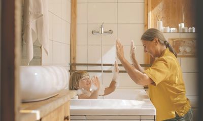 Mother helping her child take a warm bath and high-fiving him