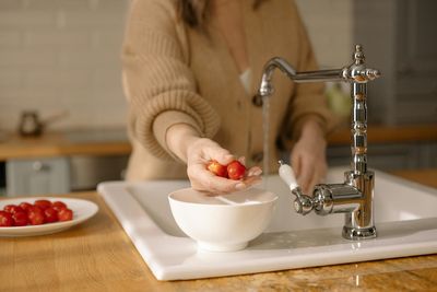 Woman washing fruits under kitchen faucet running clean tap water