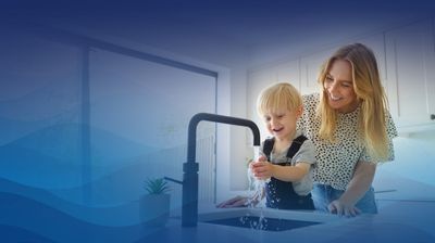 Young boy happily washing his hands at kitchen faucet, accompanied by his mother